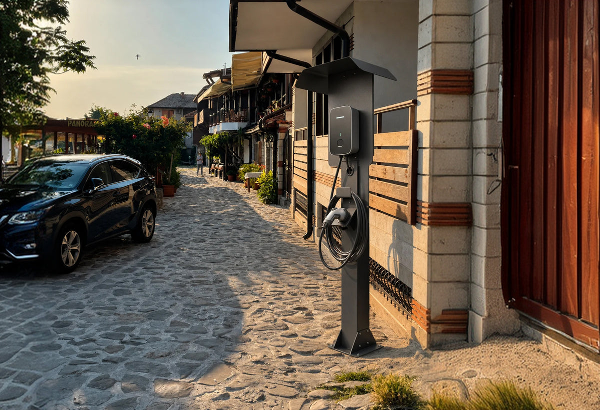 Freistehende dunkle Wallbox-Ladesäule mit Schutzdach auf einer gepflasterten Straße in einer historischen Altstadt.